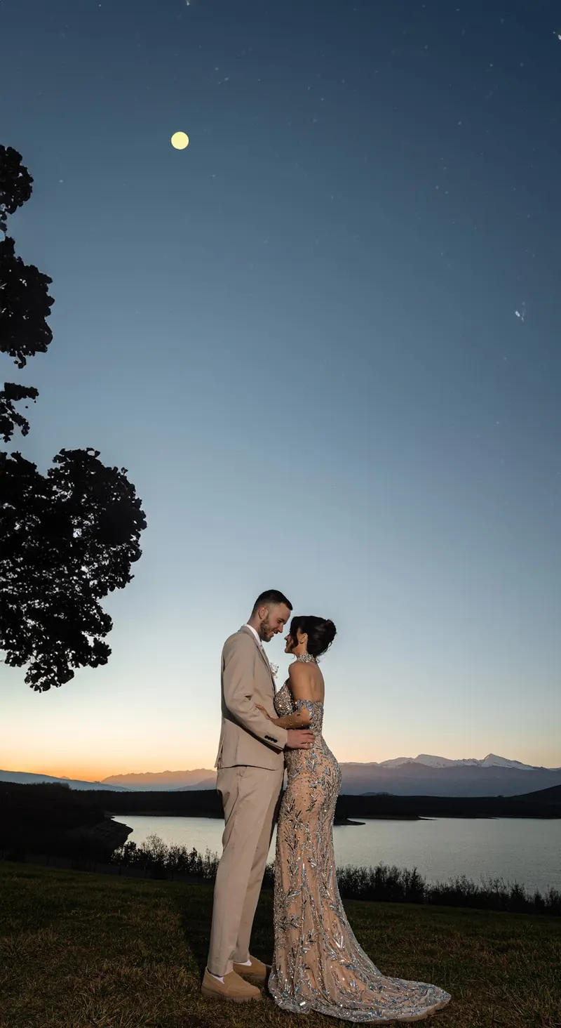 A couple standing on a hill at dusk with the moon above the lake