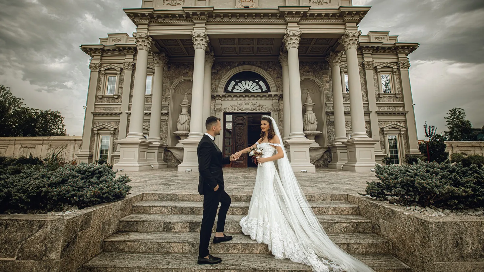 Bride and groom on the steps of a white palace, her long veil spread on the stairs