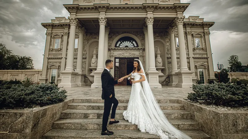 Bride and groom on the steps of a white palace, her long veil spread on the stairs