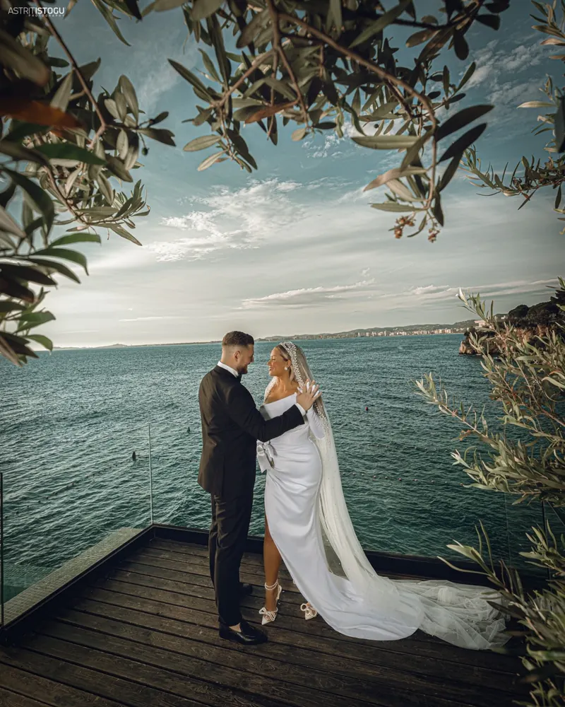 Bride and groom on a wooden pier above the sea, framed by olive branches