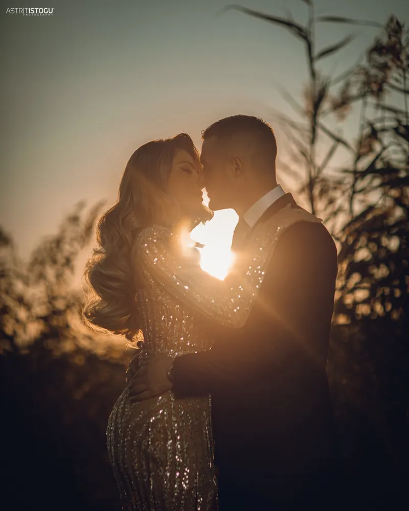 A couple about to kiss, the setting sun flaring between them
