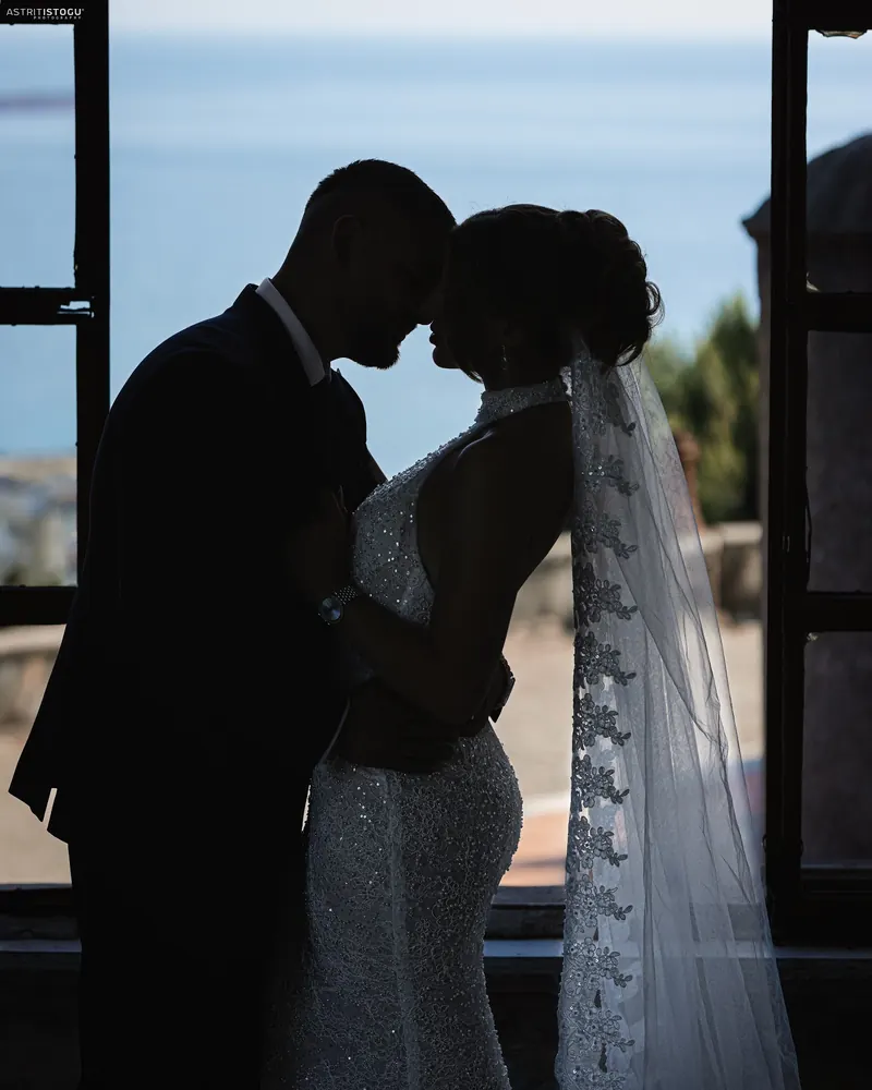 Silhouette of a bride and groom forehead to forehead at a tall window